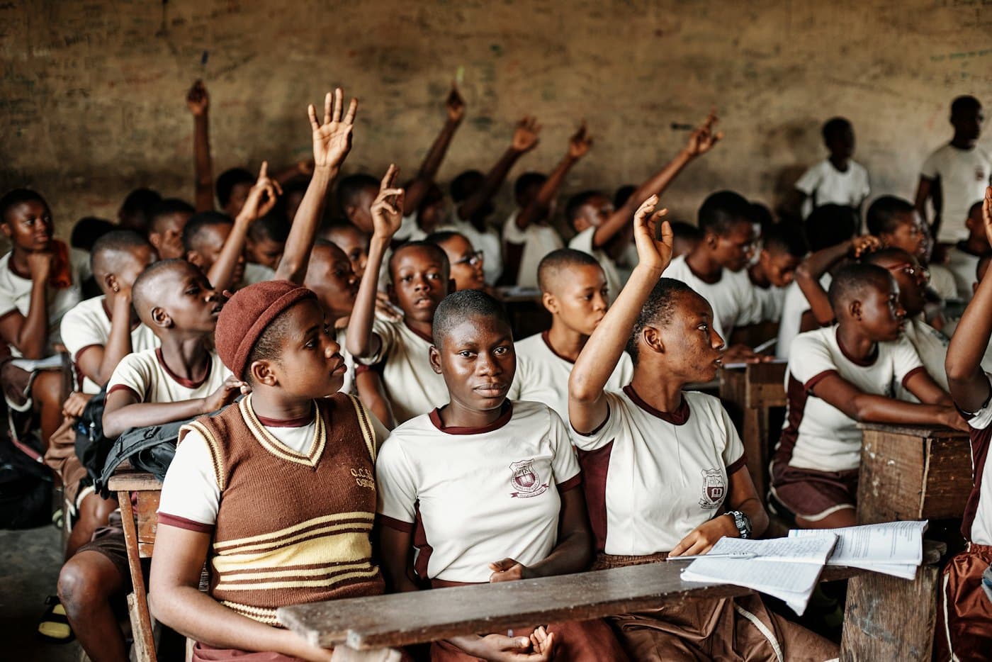 A crowded classroom of pupils raising their hands
