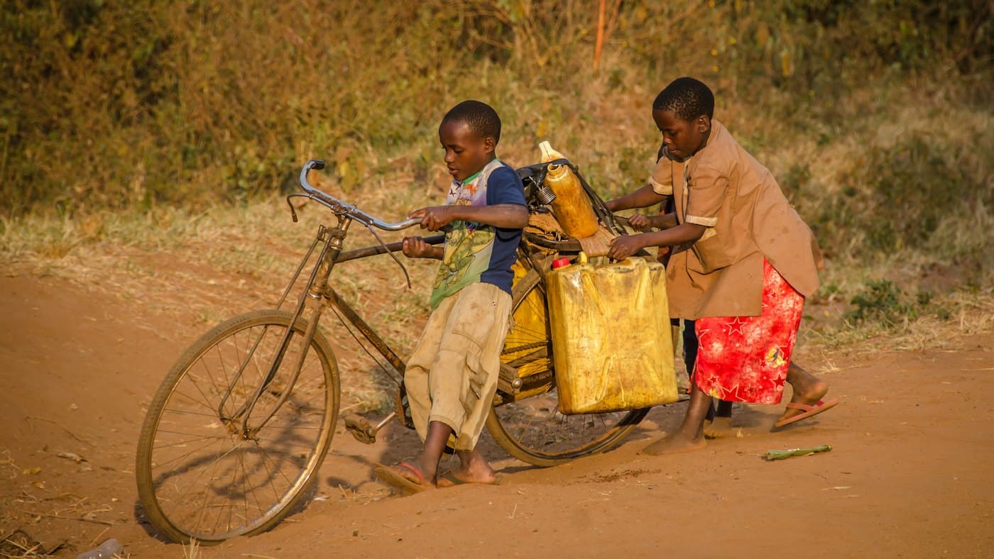 Children pushing a bicycle loaded with yellow water containers