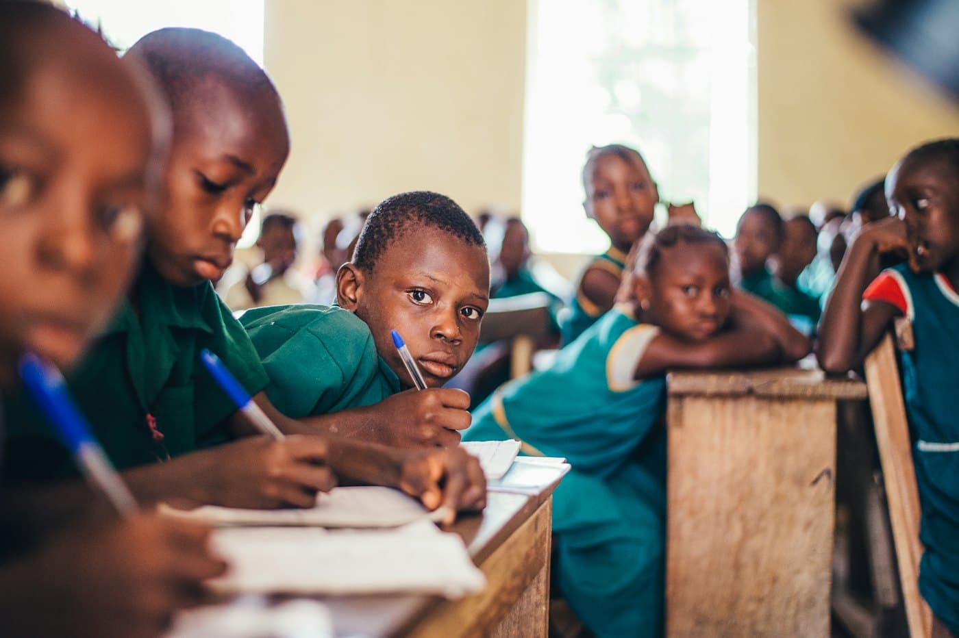 Pupils in green uniforms writing in exercise books